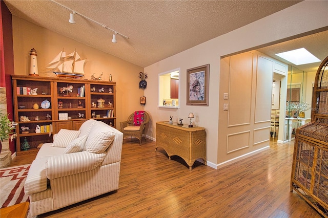 living area featuring wood finished floors, baseboards, track lighting, a textured ceiling, and lofted ceiling with skylight