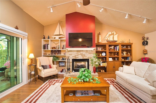 living room featuring a fireplace with raised hearth, a textured ceiling, lofted ceiling, and wood finished floors