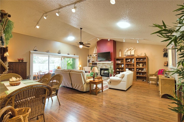 living room with a textured ceiling, wood finished floors, a stone fireplace, lofted ceiling, and ceiling fan