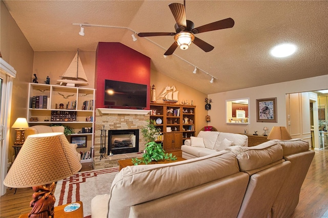 living room featuring wood finished floors, lofted ceiling, a fireplace, ceiling fan, and a textured ceiling