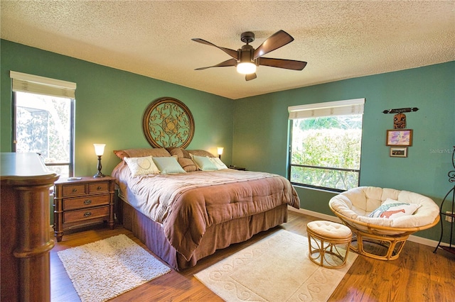 bedroom with baseboards, a textured ceiling, wood finished floors, and a ceiling fan