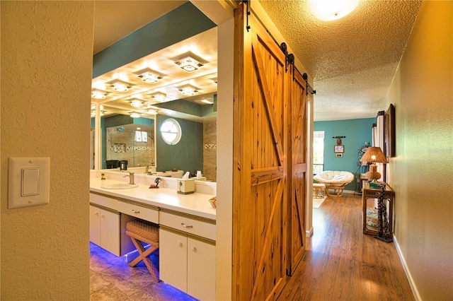 full bath featuring a textured ceiling, vanity, baseboards, and a textured wall