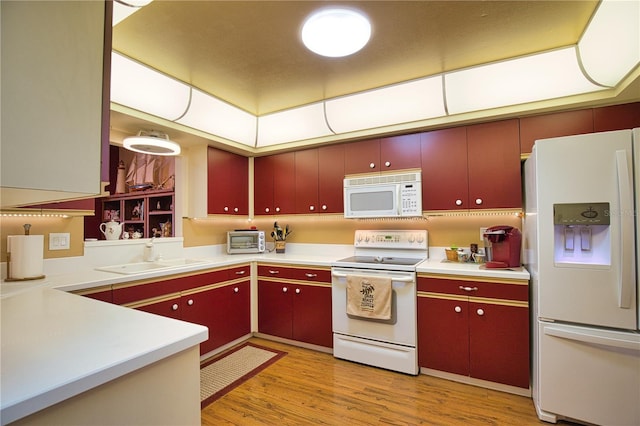 kitchen with a sink, white appliances, light wood finished floors, and red cabinets