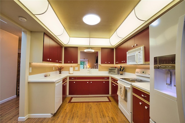 kitchen featuring white appliances, light wood finished floors, a tray ceiling, a sink, and red cabinets