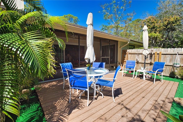 wooden deck featuring outdoor dining space, fence, and a sunroom