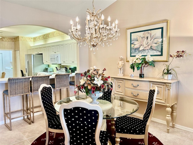 dining space featuring baseboards, light tile patterned floors, arched walkways, a notable chandelier, and washer / clothes dryer