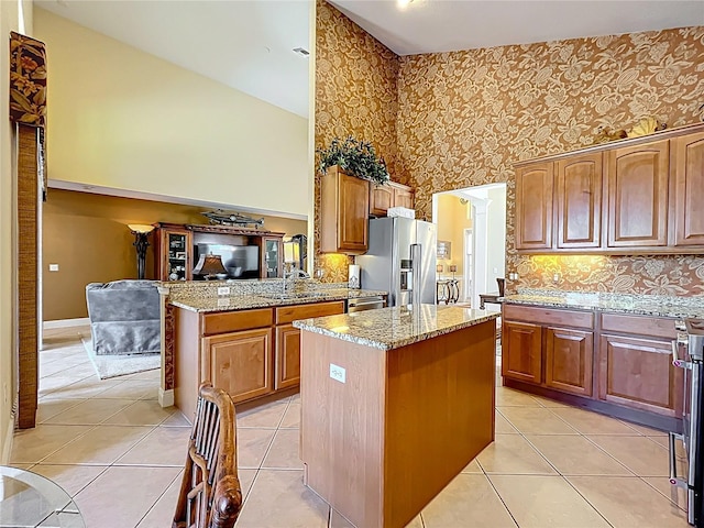 23901 Waverly Cir, Venice, FL 34293 - kitchen featuring stainless steel refrigerator with ice dispenser, high vaulted ceiling, a kitchen island, light stone countertops, and brown cabinets