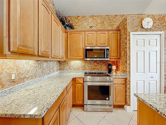 23901 Waverly Cir, Venice, FL 34293 - kitchen with stainless steel appliances, wallpapered walls, light stone counters, and light tile patterned floors