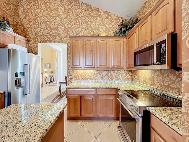 23901 Waverly Cir, Venice, FL 34293 - kitchen with stainless steel appliances, wallpapered walls, light tile patterned flooring, light stone counters, and lofted ceiling