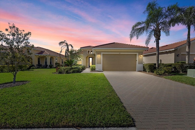 mediterranean / spanish house with an attached garage, stucco siding, a front lawn, a tiled roof, and decorative driveway