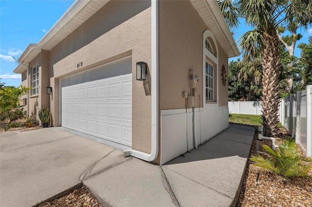 view of side of property with stucco siding, an attached garage, driveway, and fence