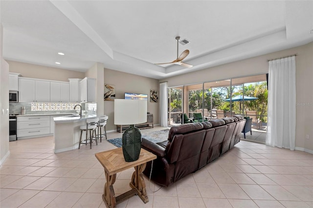 living room with visible vents, a tray ceiling, recessed lighting, light tile patterned floors, and baseboards