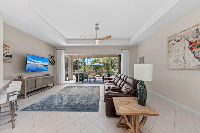 living room with tile patterned floors, a tray ceiling, baseboards, and a ceiling fan