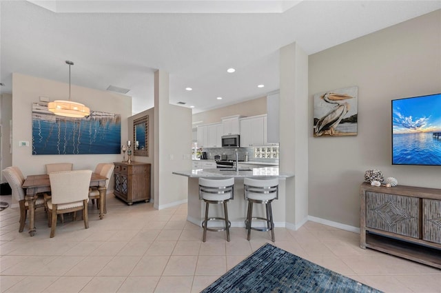 kitchen featuring tasteful backsplash, stainless steel microwave, light countertops, light tile patterned floors, and white cabinets