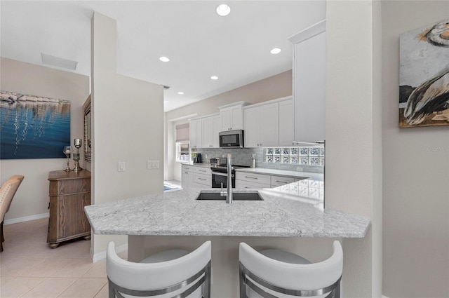 kitchen with light stone counters, a sink, decorative backsplash, appliances with stainless steel finishes, and white cabinetry