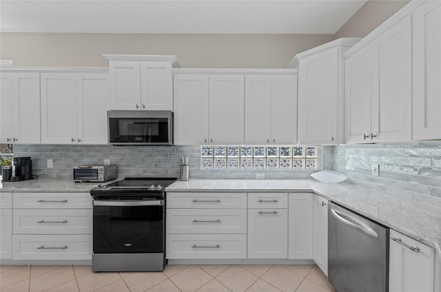 kitchen featuring white cabinetry, stainless steel appliances, light tile patterned floors, decorative backsplash, and light stone countertops