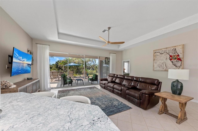 tiled living area with a raised ceiling and a ceiling fan