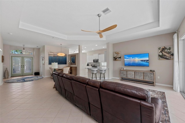 living area with light tile patterned floors, a tray ceiling, visible vents, and a ceiling fan