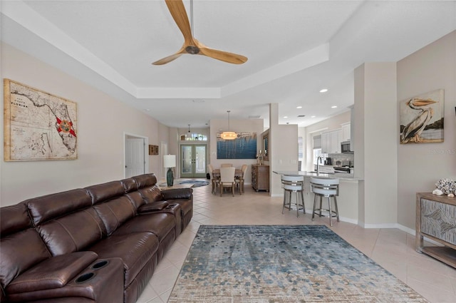 living area with baseboards, light tile patterned floors, recessed lighting, a raised ceiling, and a ceiling fan