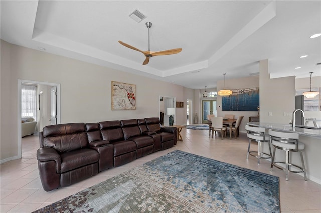 living room featuring visible vents, baseboards, light tile patterned floors, a raised ceiling, and a ceiling fan