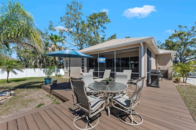 deck with outdoor dining space, fence, a yard, and a sunroom