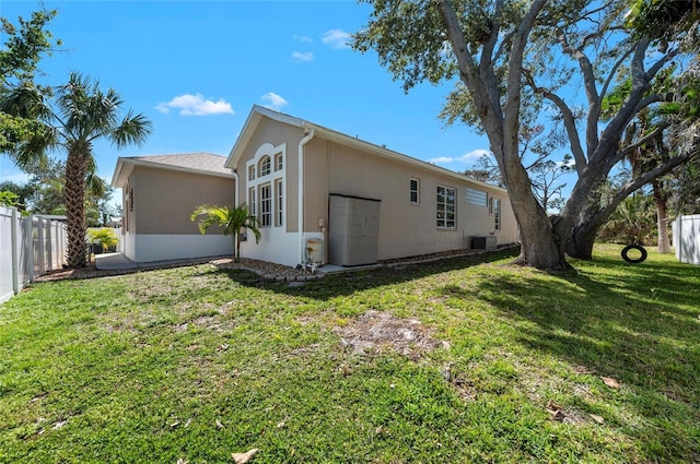 view of side of property with cooling unit, a lawn, fence, and stucco siding