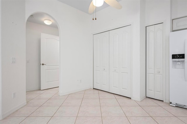 unfurnished bedroom featuring light tile patterned floors, arched walkways, white refrigerator with ice dispenser, and ceiling fan