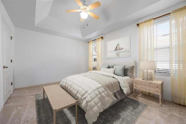 bedroom featuring a tray ceiling, a ceiling fan, baseboards, and light carpet