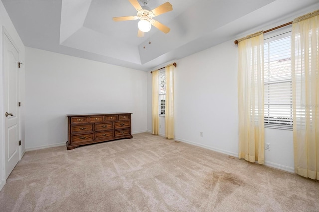 unfurnished bedroom featuring baseboards, multiple windows, a raised ceiling, and carpet floors