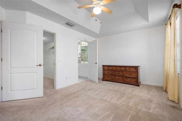 carpeted bedroom with a spacious closet, visible vents, baseboards, a tray ceiling, and ensuite bath