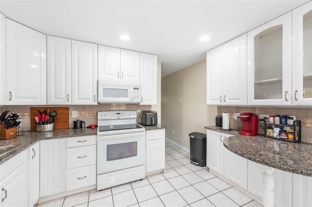 kitchen with white appliances, dark stone counters, white cabinets, glass insert cabinets, and tasteful backsplash