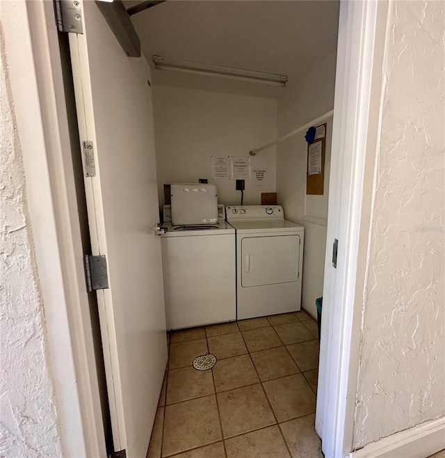 washroom featuring a textured wall, light tile patterned flooring, laundry area, and washer and clothes dryer