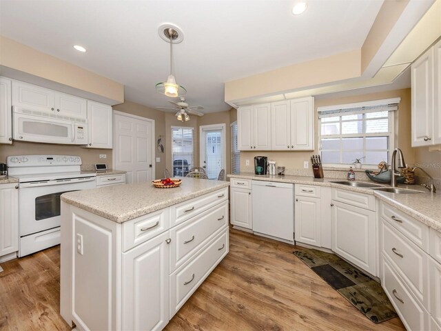 kitchen with white cabinetry, white appliances, a center island, a sink, and light wood finished floors