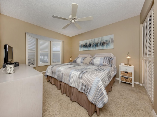 bedroom featuring baseboards, a textured ceiling, a ceiling fan, light carpet, and a closet