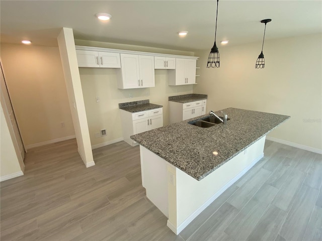 kitchen with an island with sink, light wood-type flooring, recessed lighting, white cabinetry, and a sink