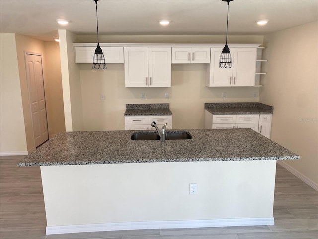 kitchen with a sink, light wood-style flooring, an island with sink, and white cabinets