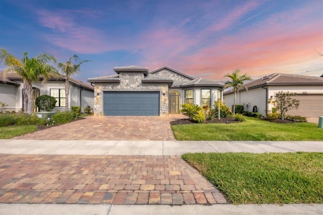 mediterranean / spanish house with a front lawn, a garage, stone siding, a tile roof, and decorative driveway