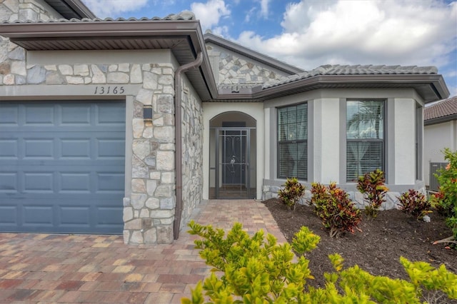 entrance to property with stucco siding, stone siding, and an attached garage