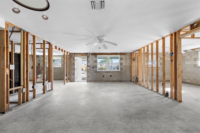 miscellaneous room with visible vents, concrete flooring, ceiling fan, and concrete block wall