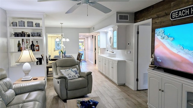 interior space featuring light wood finished floors, visible vents, open floor plan, ceiling fan with notable chandelier, and white cabinets