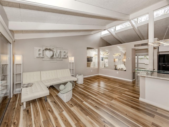 living area with a textured ceiling, lofted ceiling with beams, baseboards, and wood finished floors