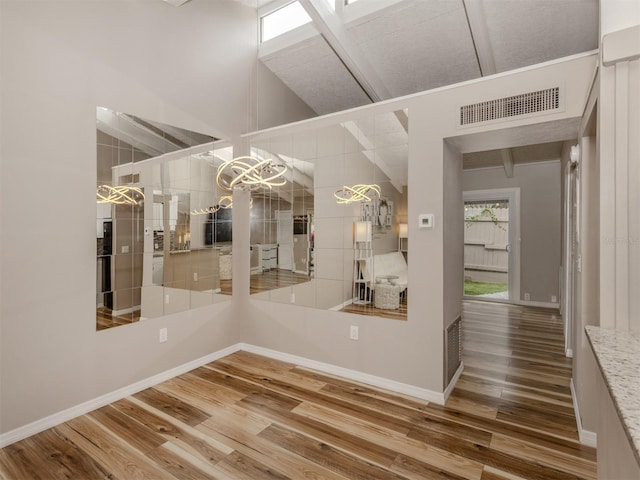 interior space with wood finished floors, visible vents, baseboards, an inviting chandelier, and a towering ceiling