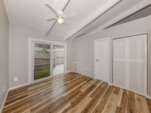 unfurnished bedroom with baseboards, lofted ceiling with beams, wood finished floors, a closet, and a ceiling fan