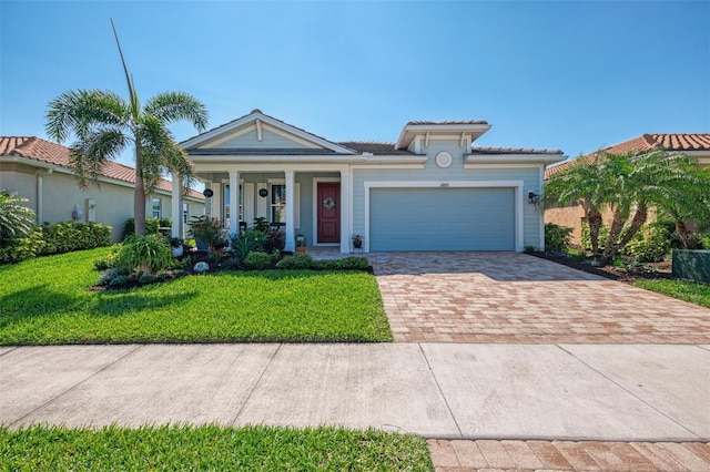 view of front of property with a tile roof, decorative driveway, a front yard, covered porch, and a garage