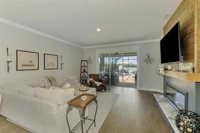 living area featuring a glass covered fireplace, baseboards, visible vents, ornamental molding, and dark wood-style flooring
