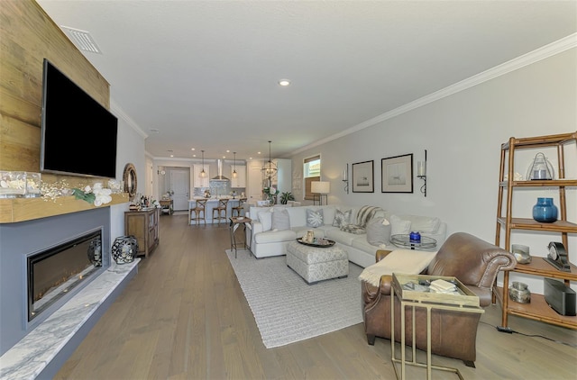 living room with visible vents, crown molding, wood finished floors, recessed lighting, and a glass covered fireplace