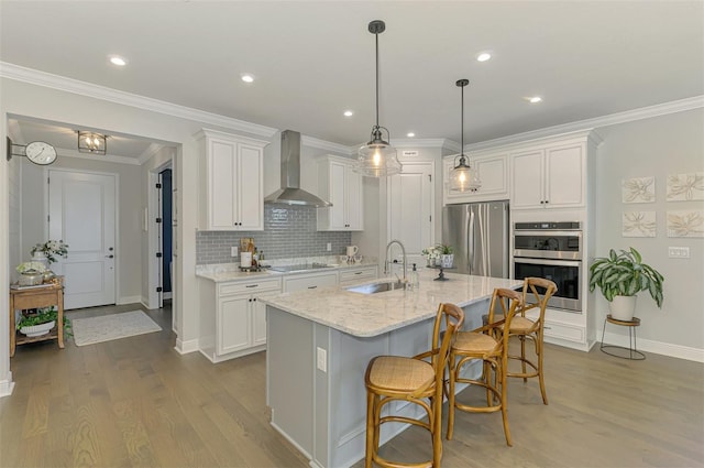 kitchen featuring wall chimney range hood, a sink, white cabinets, and appliances with stainless steel finishes