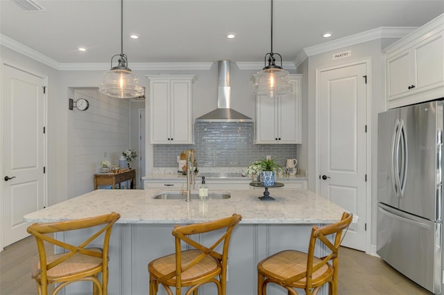 kitchen featuring crown molding, freestanding refrigerator, white cabinetry, wall chimney exhaust hood, and light wood-style floors