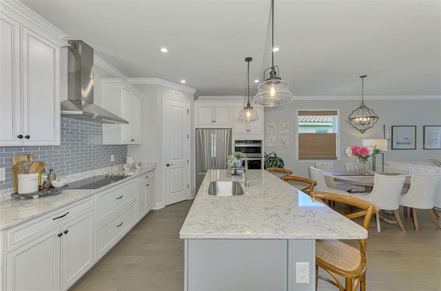 kitchen with crown molding, a breakfast bar, a sink, wall chimney range hood, and appliances with stainless steel finishes