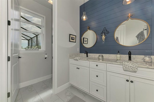 bathroom with marble finish floor, baseboards, double vanity, and a sink